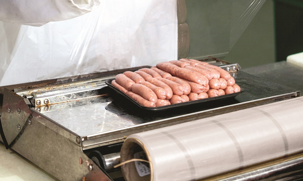Female butcher packing raw sausages at meat factory
